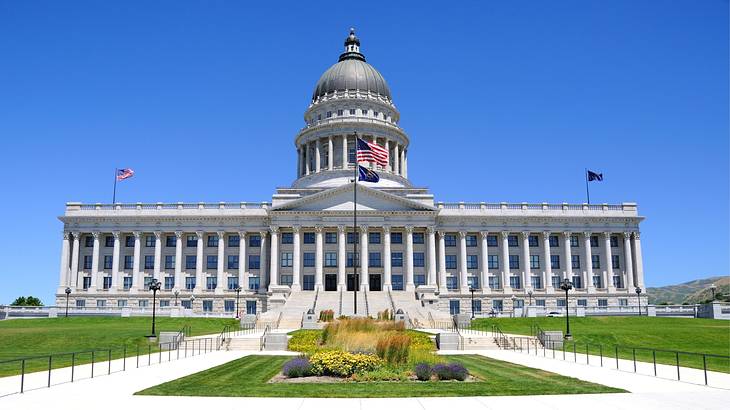 A white state capitol building with a domed roof in the middle and grass in front