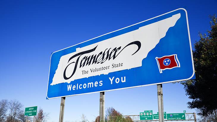 Blue road sign on highway: "Tennessee, The Volunteer State, Welcomes You"