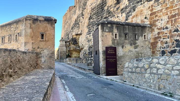 A wall fortification with open brown doors and a road in between, beside a rock face