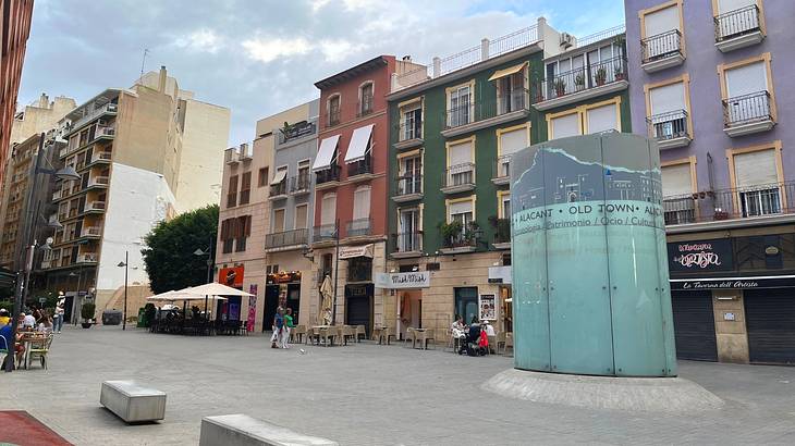 A square lined with colourful buildings, with a blue curved structure on the right