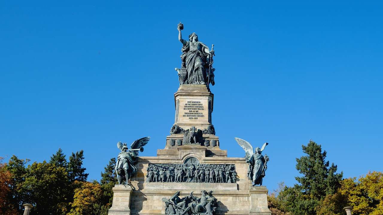 A statue of a woman holding a sword with smaller statues below it under a blue sky