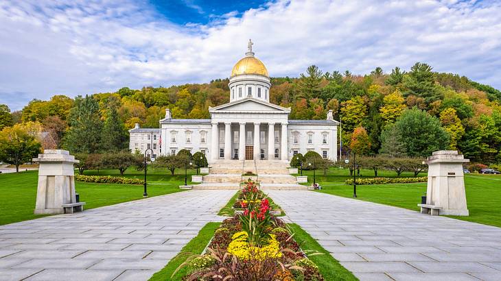 A state capitol building with a gold dome roof next to trees and a garden