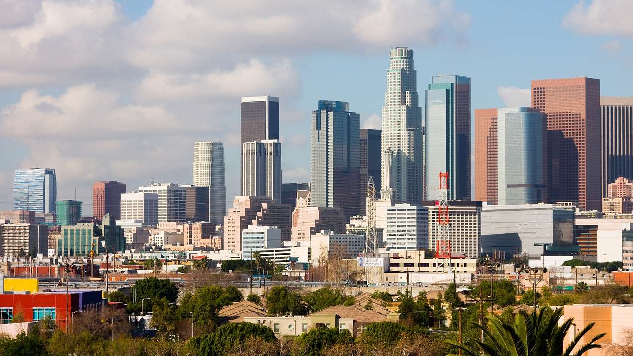 The LA city skyline with greenery in front of it under a blue sky with clouds