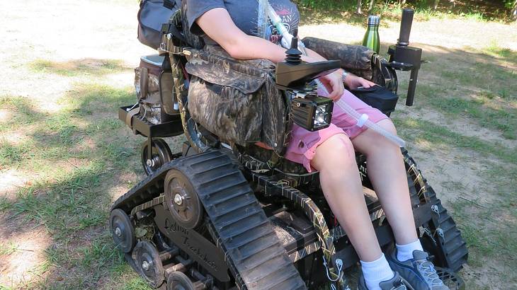A woman sitting in an adapted wheelchair that has tank tracks for wheels