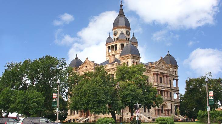 A regal building with domed roofs surrounded by green trees and grass