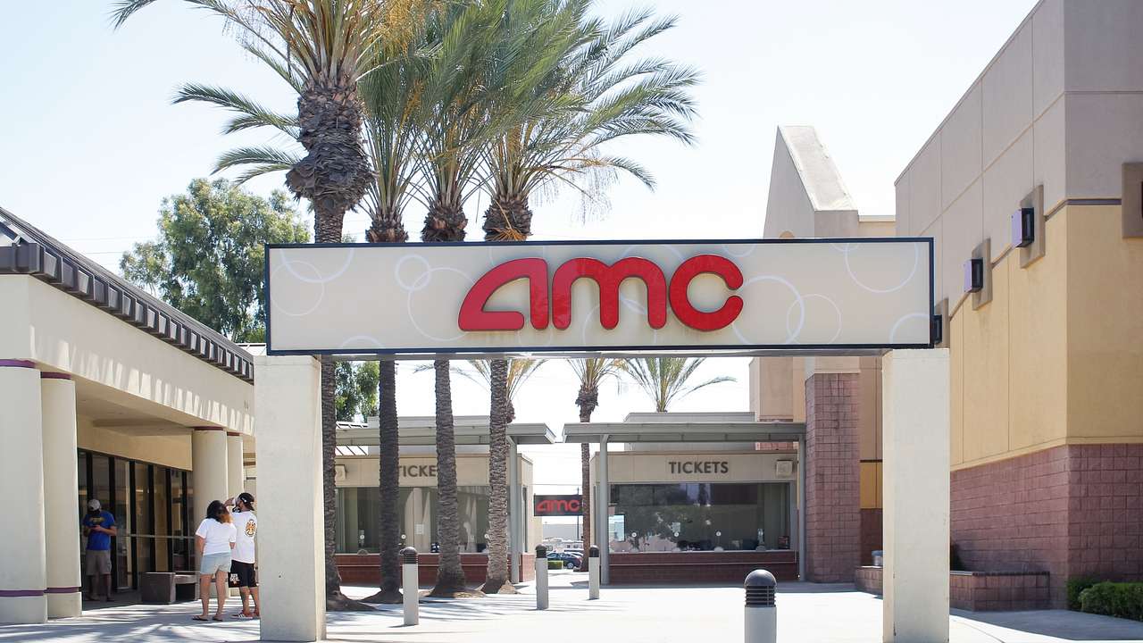 A sign that says "AMC" in front of palm trees and the entry to a movie theater