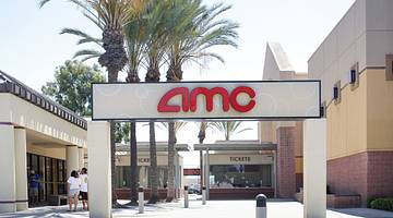 A sign that says "AMC" in front of palm trees and the entry to a movie theater