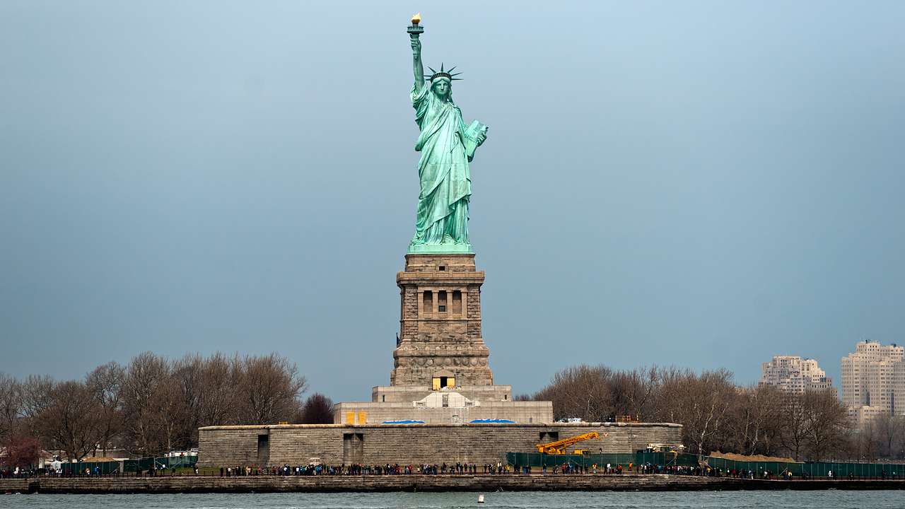 The Statue of Liberty standing on an island with trees either side and water in front