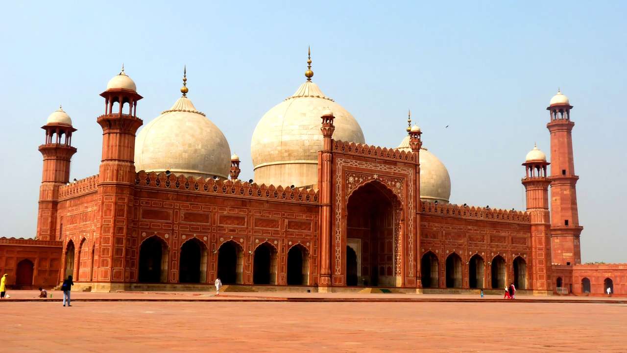 The exterior of a red-orange mosque with towers and dome structures