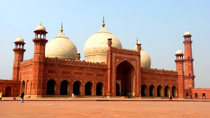 The exterior of a red-orange mosque with towers and dome structures