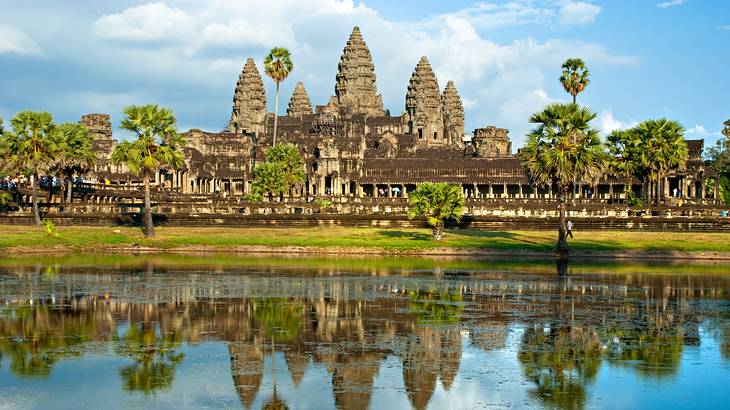 An ancient temple next to trees, grass, and water under a blue sky with some clouds