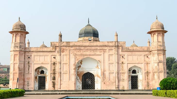 A pink-ish fort structure with two towers and a dome next to greenery and a pool