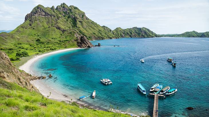 A turquoise lagoon with boats on it, surrounded by a greenery-covered hill