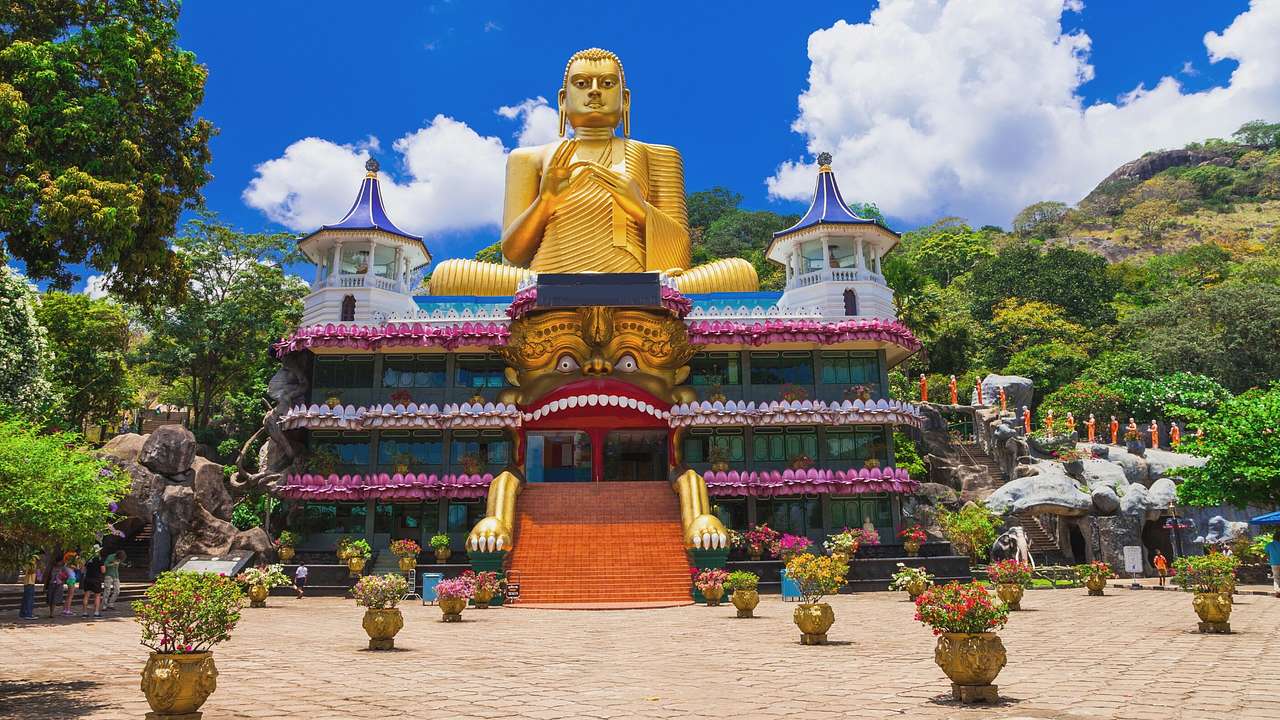 A golden Buddha statue atop a temple structure with greenery and flowers around it