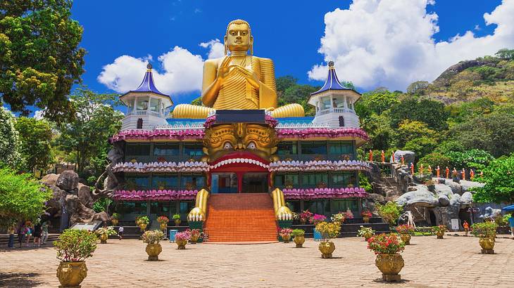 A golden Buddha statue atop a temple structure with greenery and flowers around it