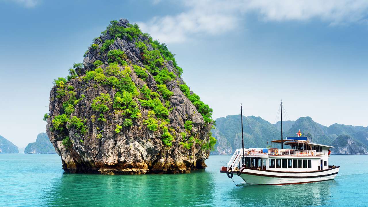 Turquoise water with a large greenery-covered cliff and a white boat in the middle
