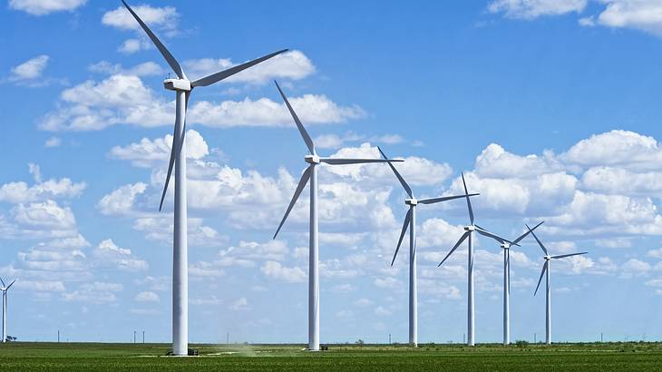 A row of white wind turbines in a field of green grass on a nice day