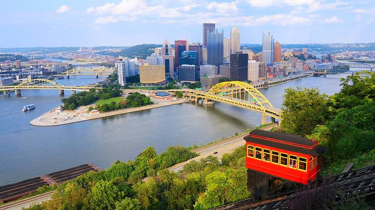 A view of Pittsburgh with a red incline car, yellow bridges over water, and buildings