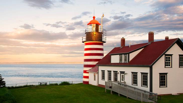 A red and white lighthouse and building on a grassy hill by the water