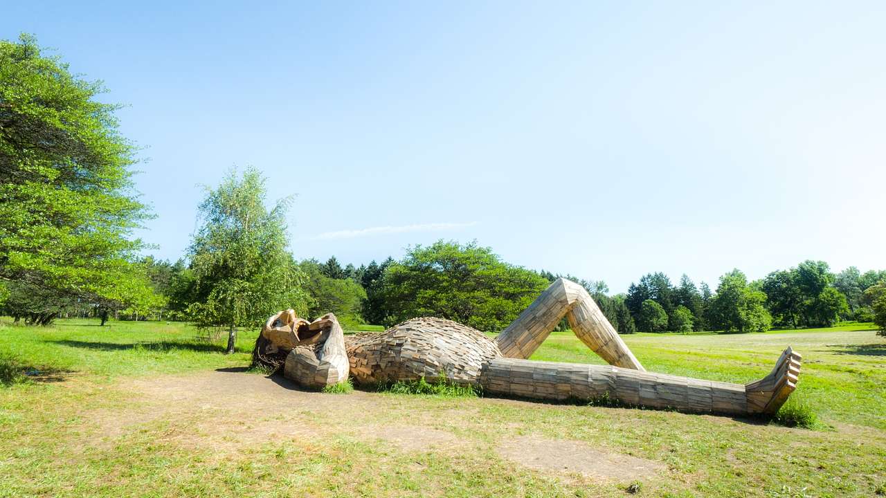 A wooden sculpture of a person lying down surrounded by grass and green trees