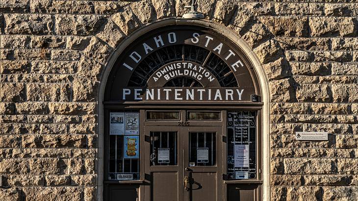 A brick wall with a brown arched door and an "Idaho State Penitentiary" sign