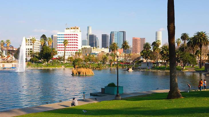 A park with a large lake with a fountain in the middle next to city buildings