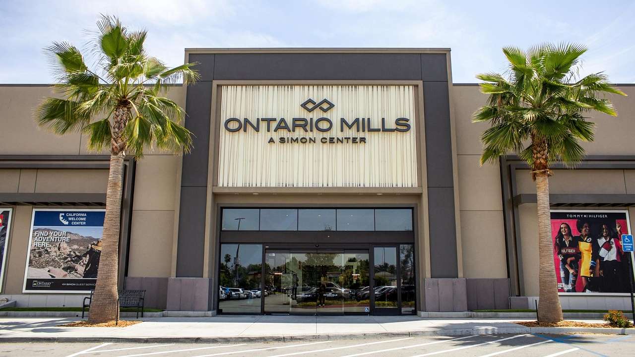The exterior of a luxury shopping mall with an "Ontario Mills" sign and palm trees