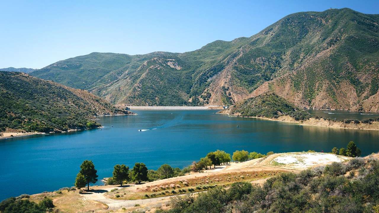 A lake surrounded by trees and greenery-covered hills under a blue sky