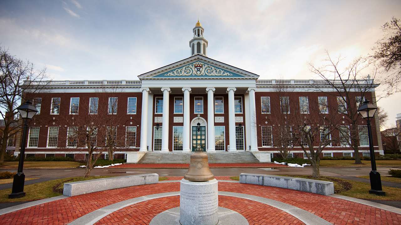 A red building with six white columns in the center facing a gold bell on a pedestal