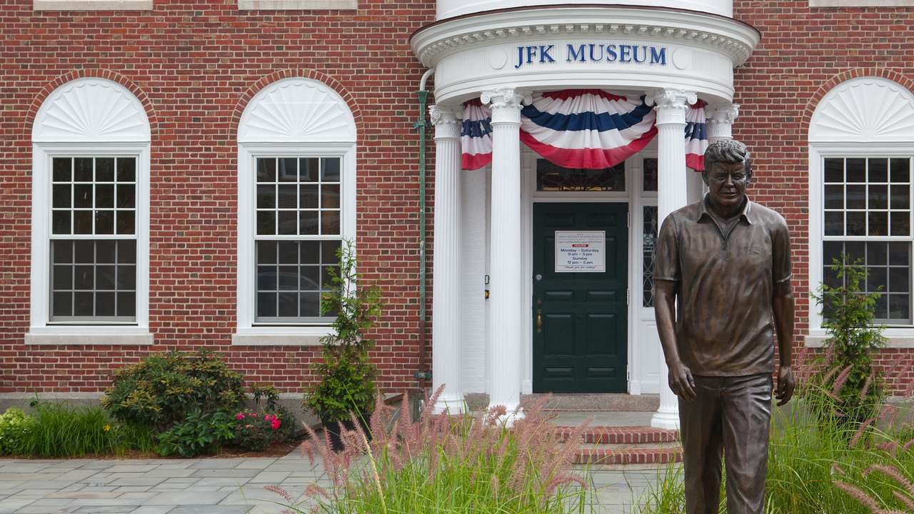 A red brick building with four columns and a statue of John F. Kennedy after it