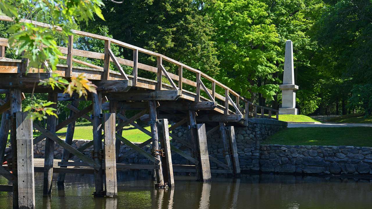 A wooden bridge over water with a monument amidst trees in the background