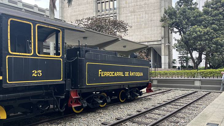 A stationed black and yellow train cart on display with a grey building behind
