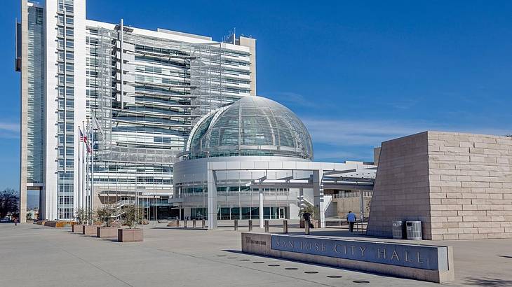 A round building with a dome, a modern building, and a "San Jose City Hall" sign