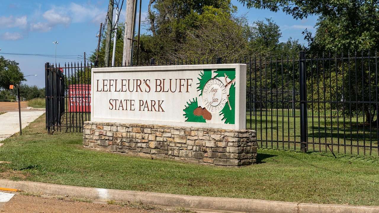 A sign that says "LeFleur's Bluff State Park" on the grass with trees behind it