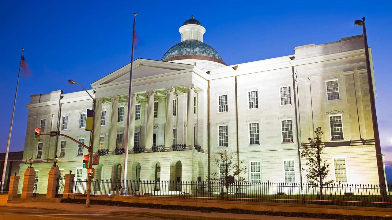 A stone state capitol building with columns and a dome illuminated at night