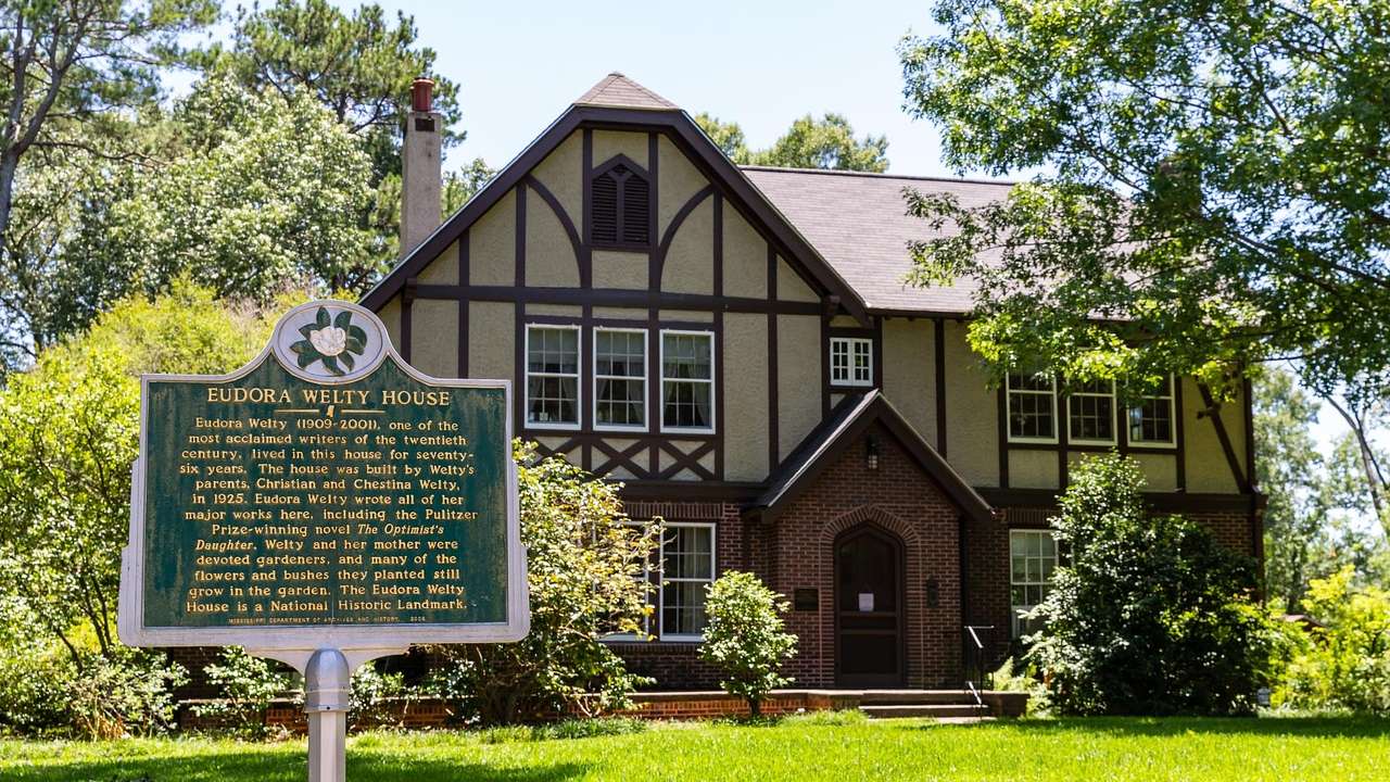 A Tudor-style house with trees, grass, and an informational plaque in front of it