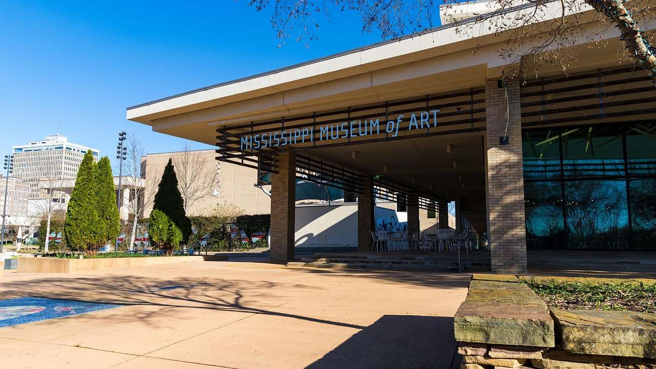 A modern building with a "Mississippi Museum of Art" sign next to a patio and trees