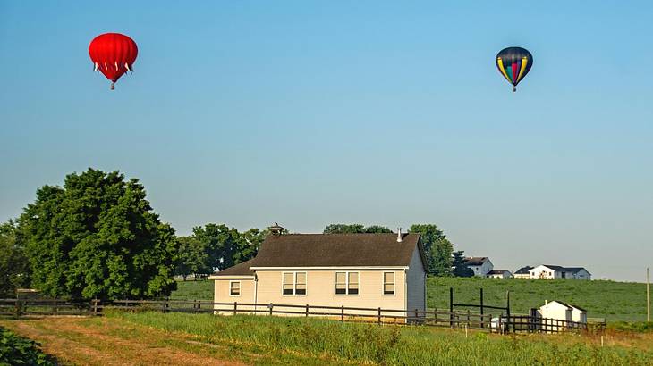 Two hot air balloons flying above a field with a small building in it