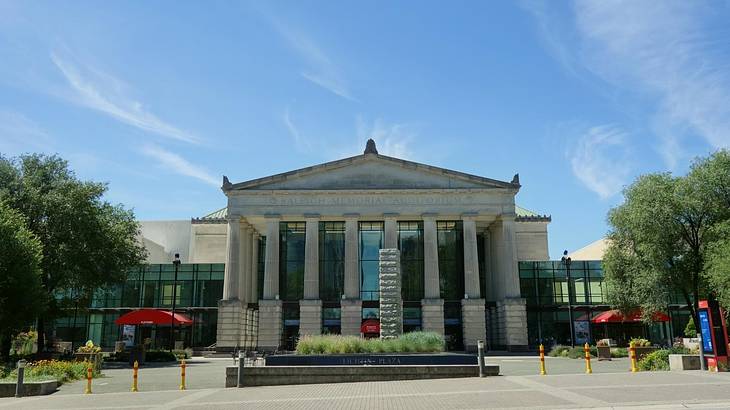 A stone building with columns next to a square and trees under a blue sky