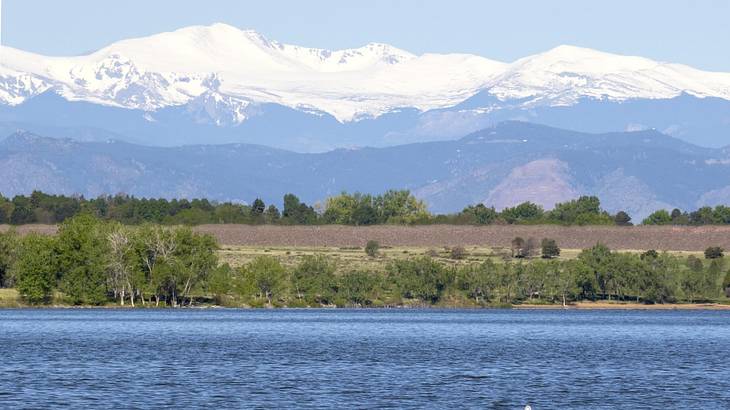 A lake next to trees and snow-covered mountains