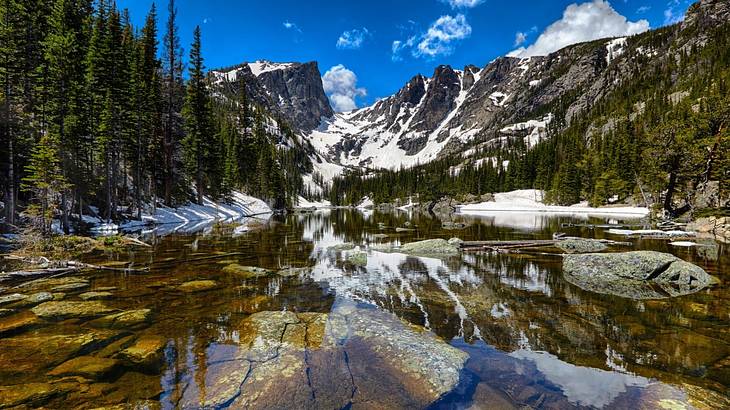 A snow-covered mountain next to a glacial lake with trees on either side