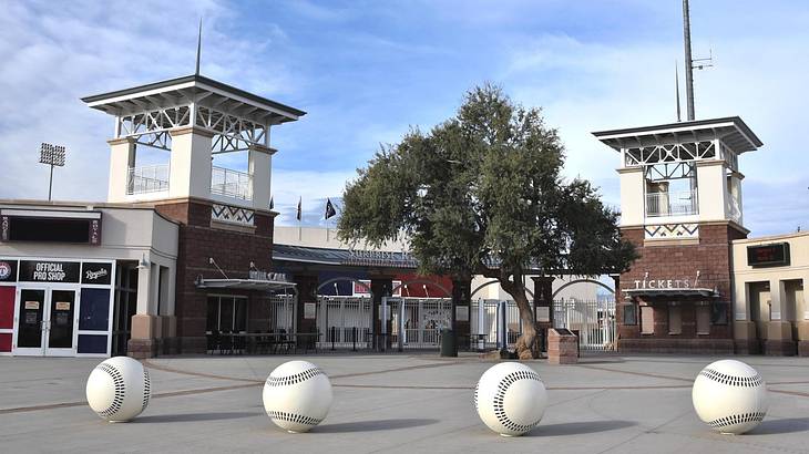 The entrance to a small stadium with two towers and baseball sculptures in front