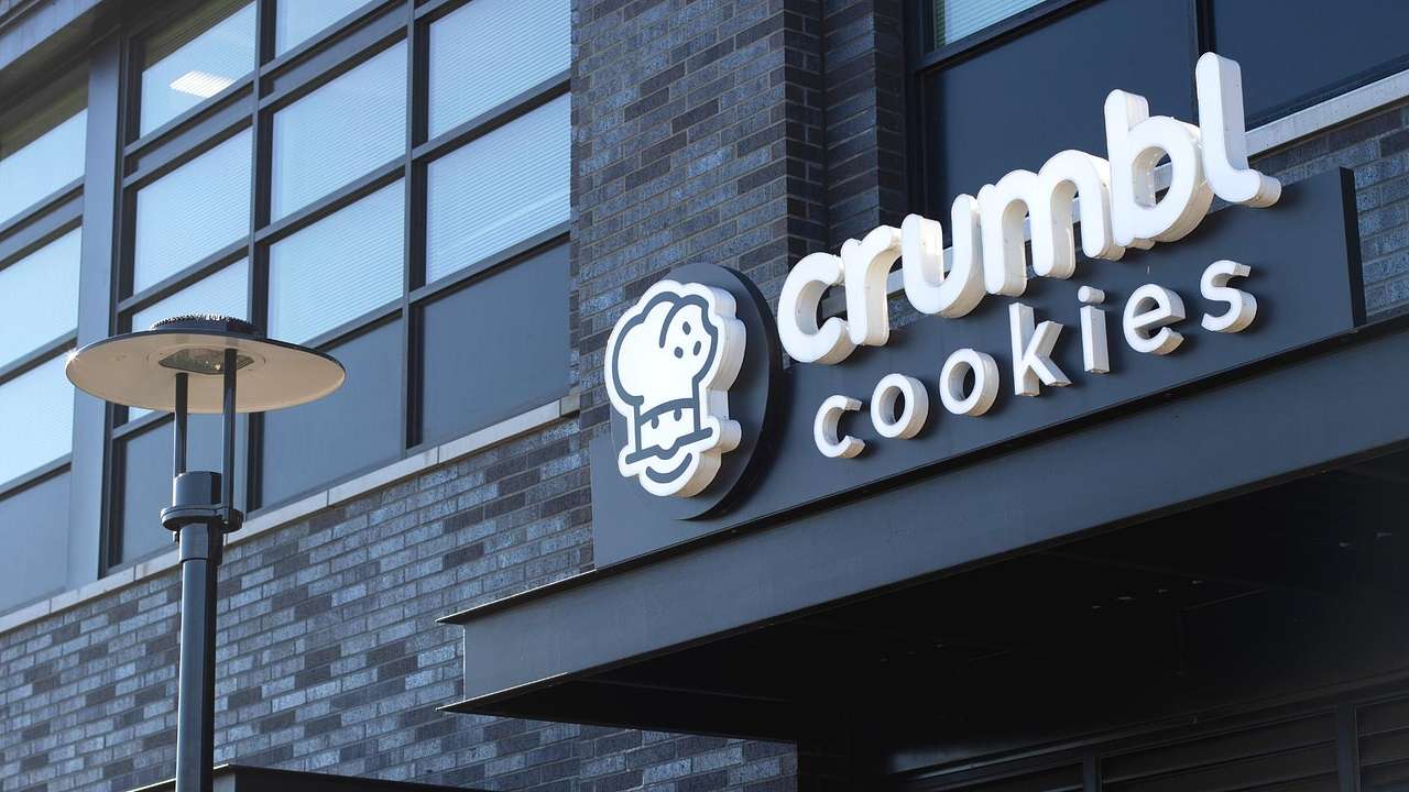 The exterior of a black brick building with a white sign that says "Crumbl Cookies"
