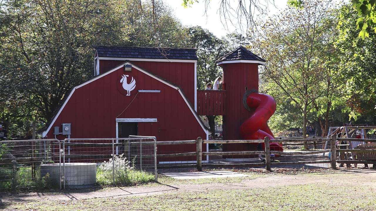 A red barn with a rooster design on it and a slide coming out of it next to grass