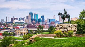 A city skyline and a grass-covered hill with a statue of a person on a horse on it