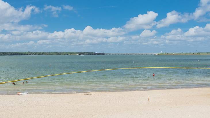 A turquoise lake next to a sandy shore under a blue sky with white clouds