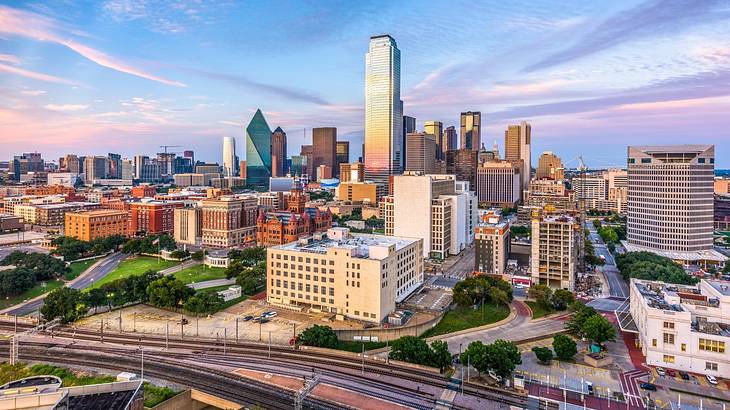 The Dallas city skyline under a pink and purple sky at sunset