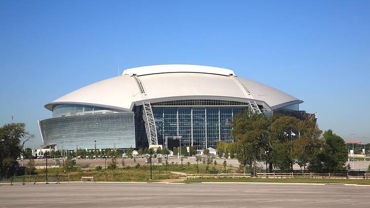 A football-shaped stadium with trees and a parking lot in front of it