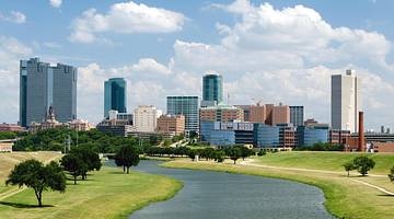 The Fort Worth city skyline next to a river, grass, and trees