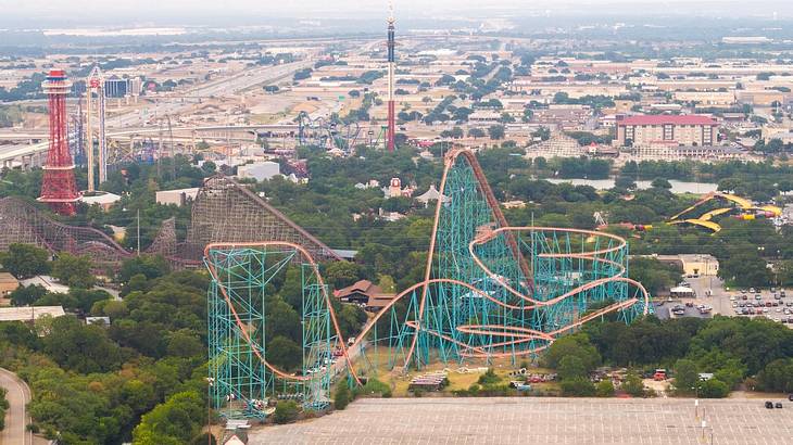 A view of a theme park with roller coasters surrounded by trees